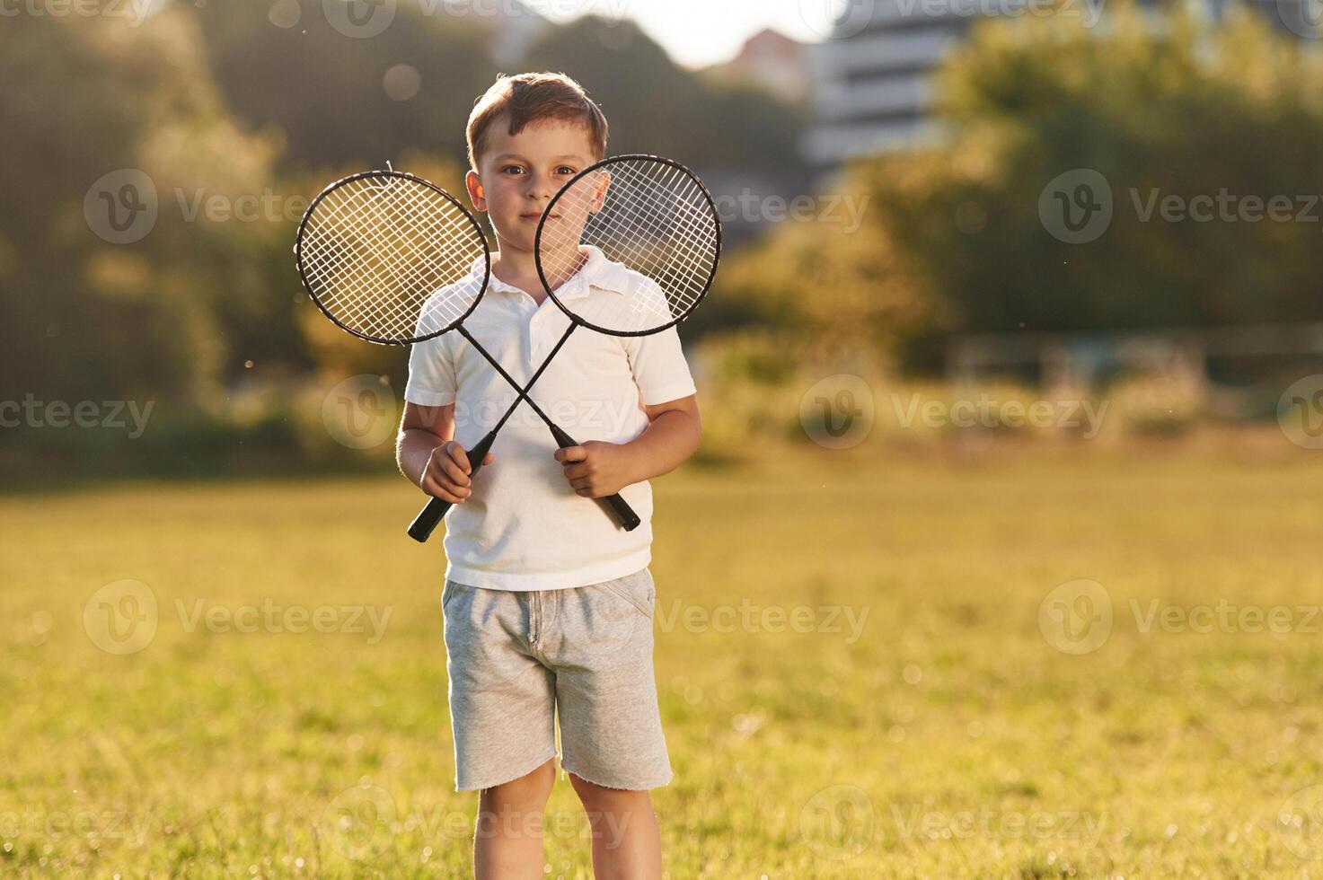 Happy little boy is with two tennis or badminton rackets on the summer field photo