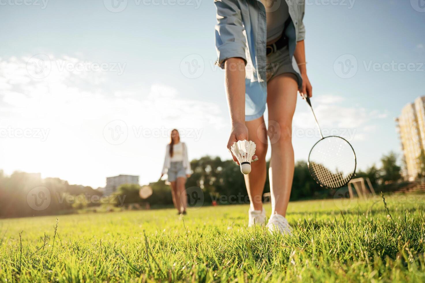 Picking up the fallen shuttlecock.. Two women are having fun, with badminton rackets, on the field photo