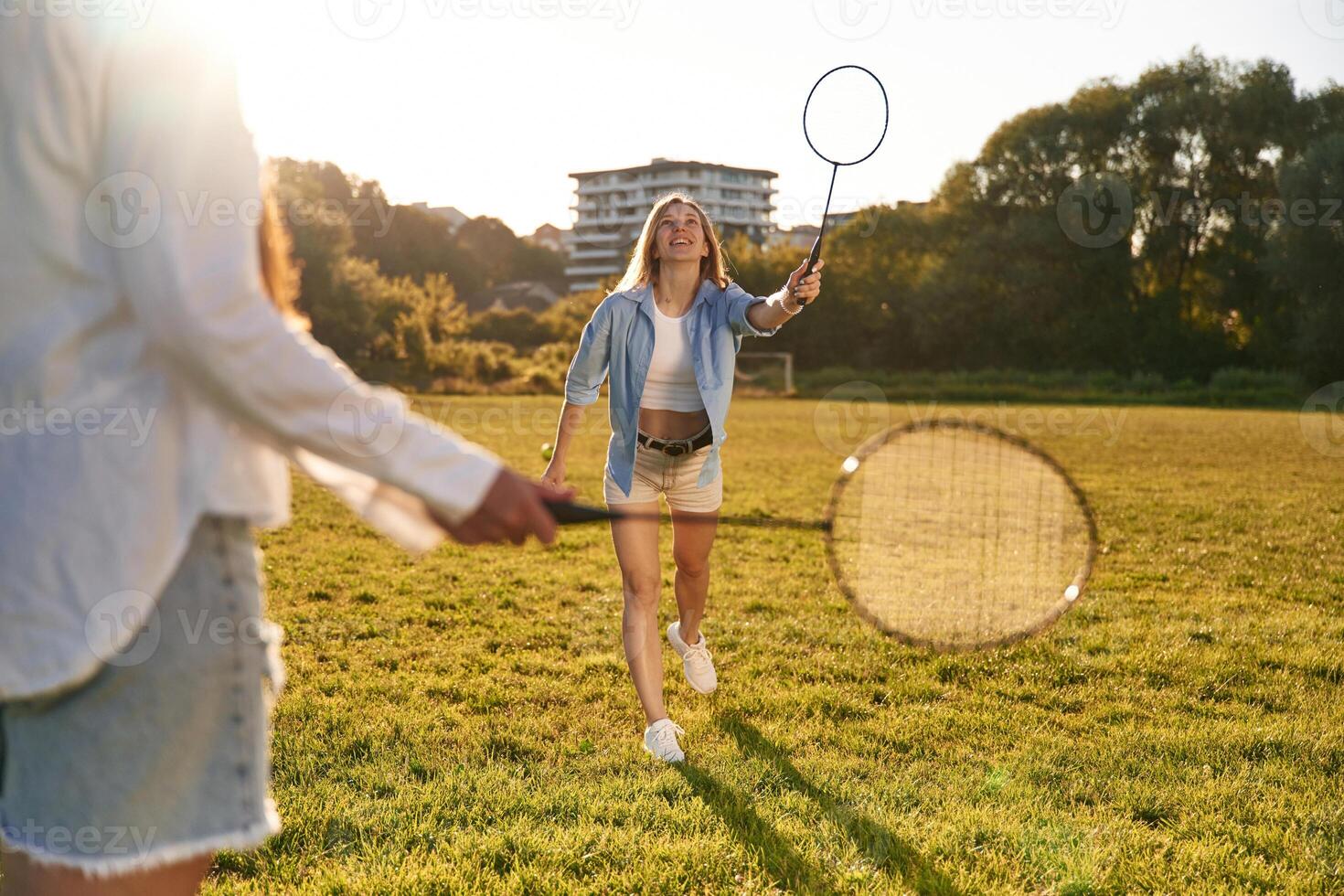 Two ,women are ,having fun, with badminton rackets, on the field photo