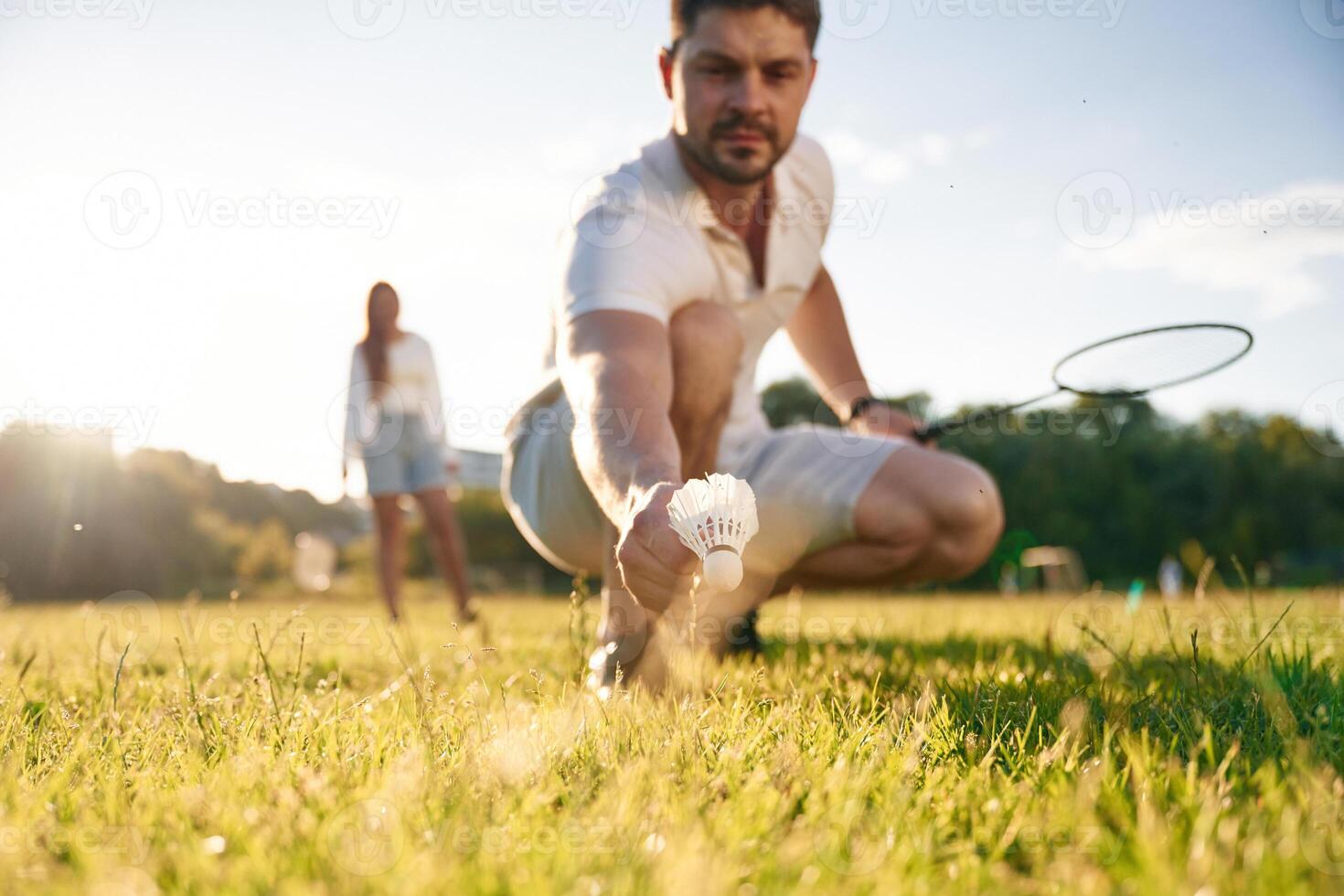 Fallen, shuttlecock, guy is taking it. Man with woman are playing badminton on the field photo