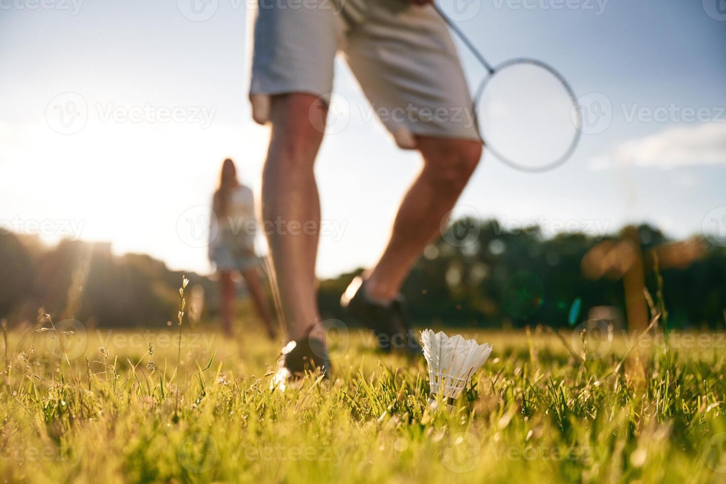 Guy is picking, up the shuttlecock. Man with woman are playing badminton on the field photo