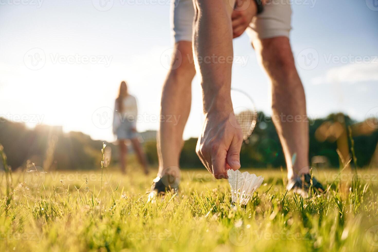 Guy, is picking up the shuttlecock. Man with woman are playing badminton on the field photo