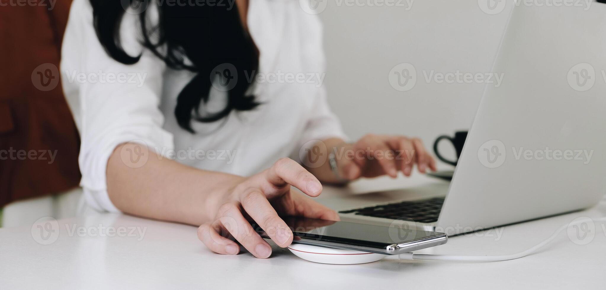 Cropped image of an office woman is charging a smartphone with a wireless charger while typing on a computer laptop. photo