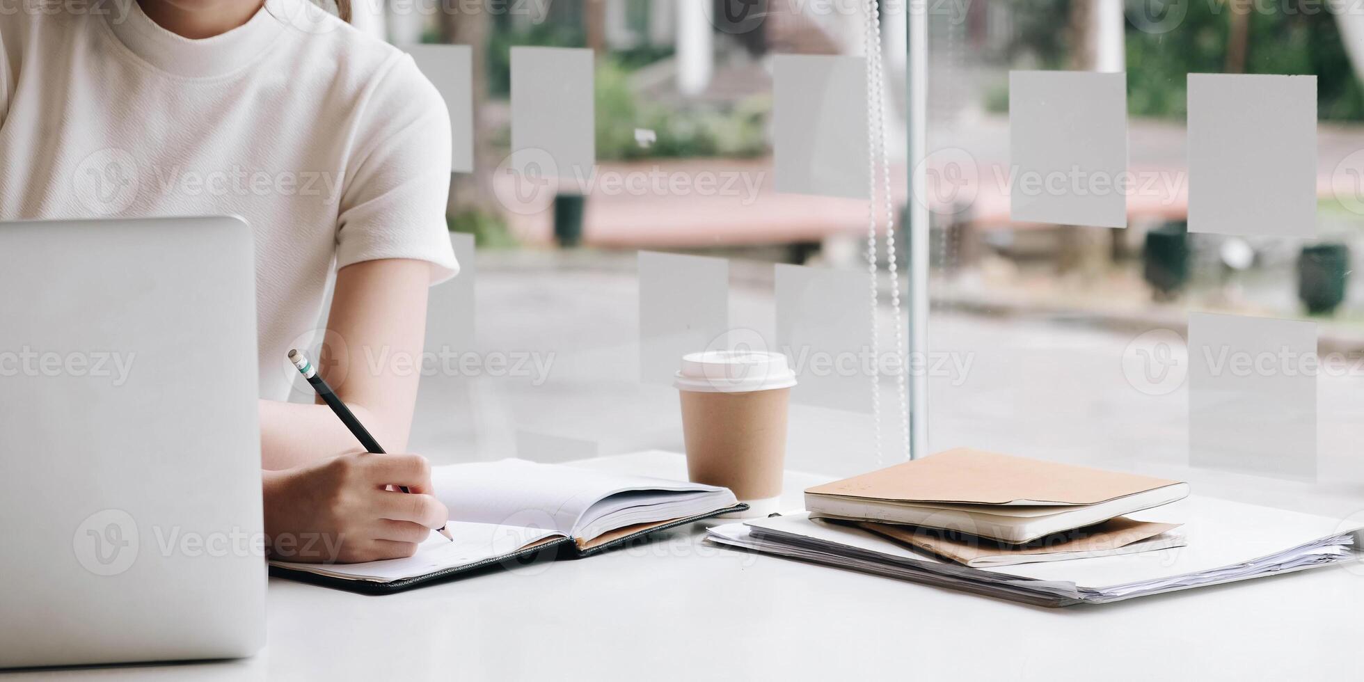 Business woman hand writing on notebook, work on laptop computer with calculator on the desk at modern home office. Online working, work at home concept photo