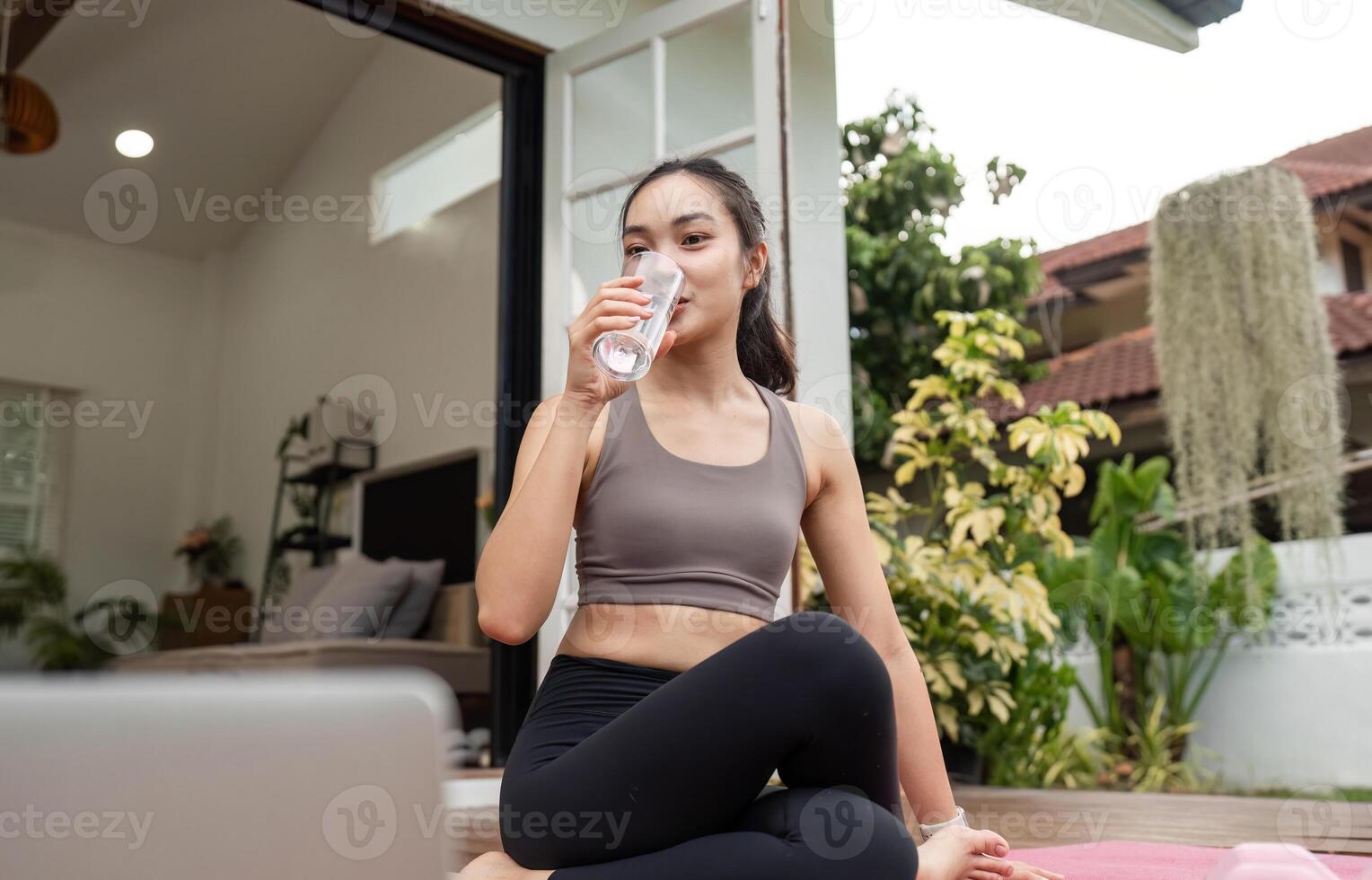 Yoga and Hydration. Young woman sipping water while practicing yoga in a serene home setting. photo