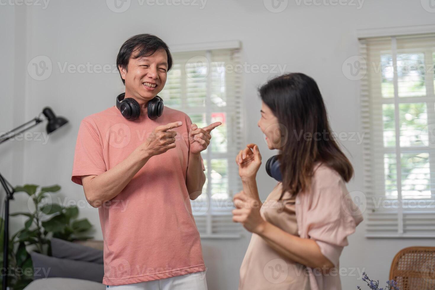 Diverse couple happily dancing in a living room with headphones and joy. photo