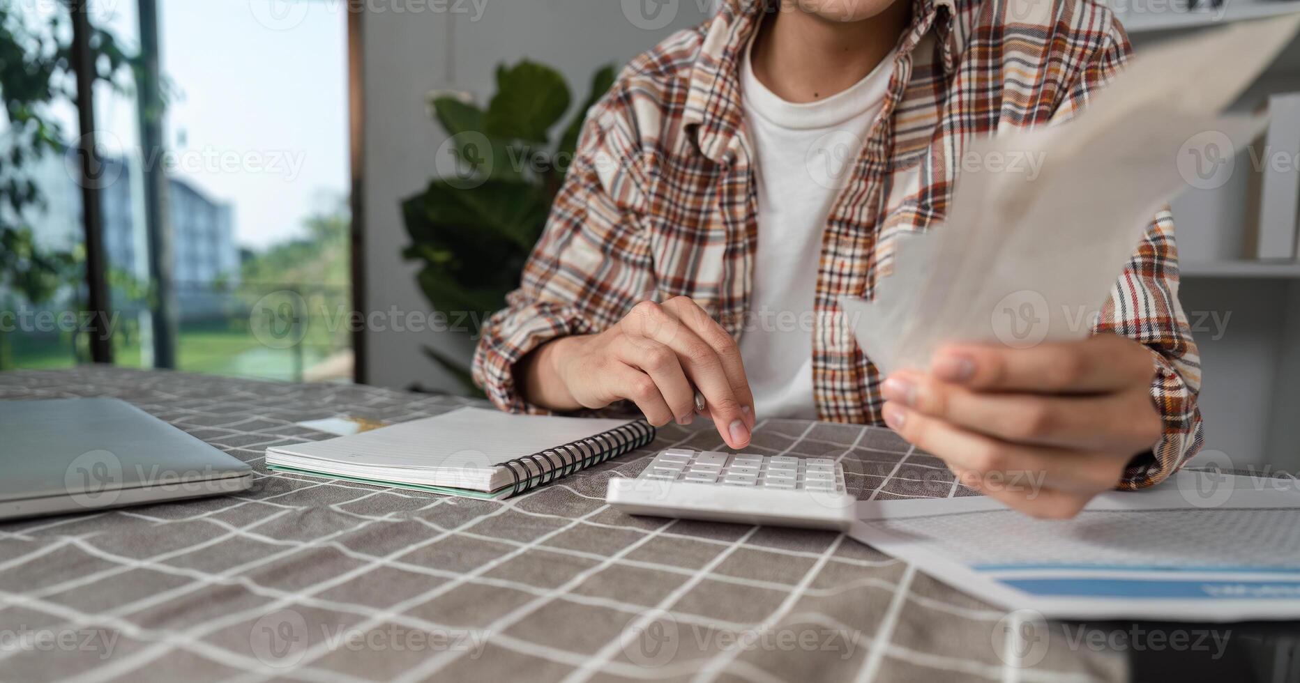 Young man managing finances with calculator and cash at home, focusing on budgeting and financial planning. photo