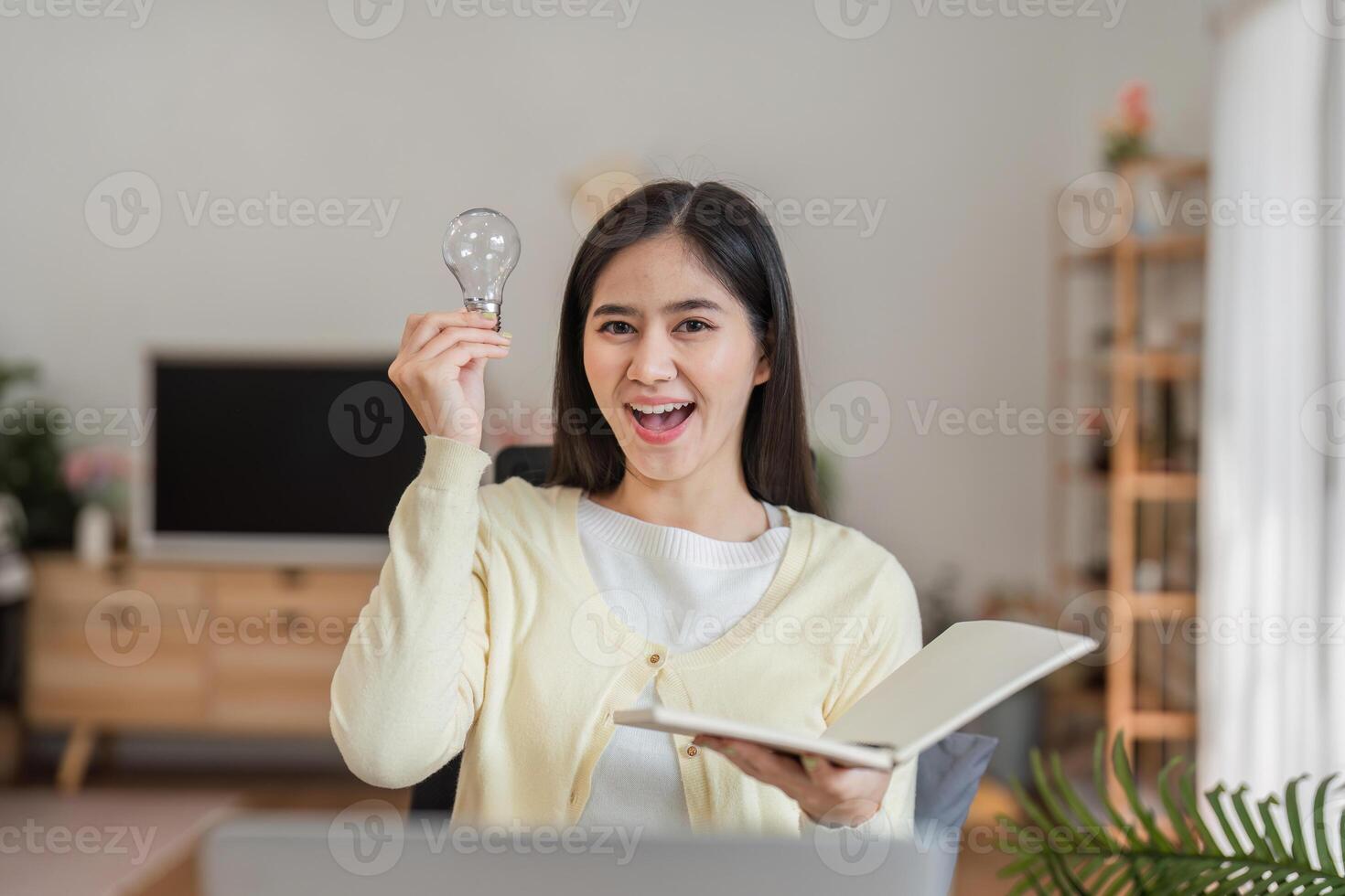 Happy woman with light bulb and book, embodying creativity in her home workspace photo