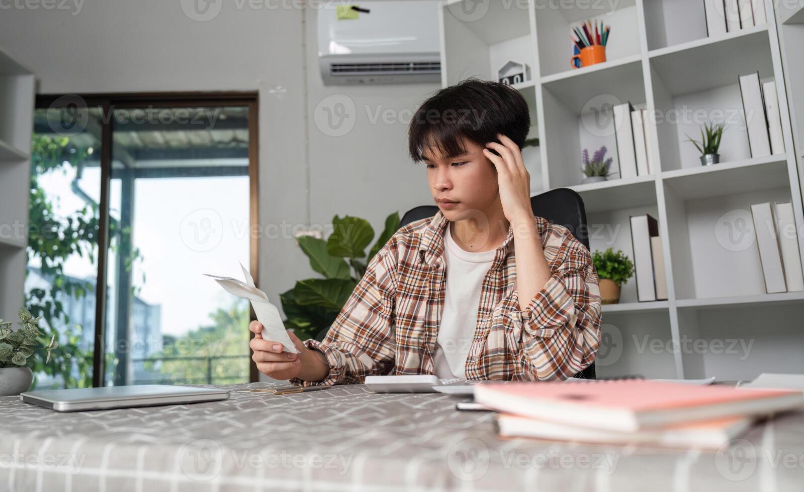 Young man feeling overwhelmed by financial documents at home office, expressing concern over budgeting. photo