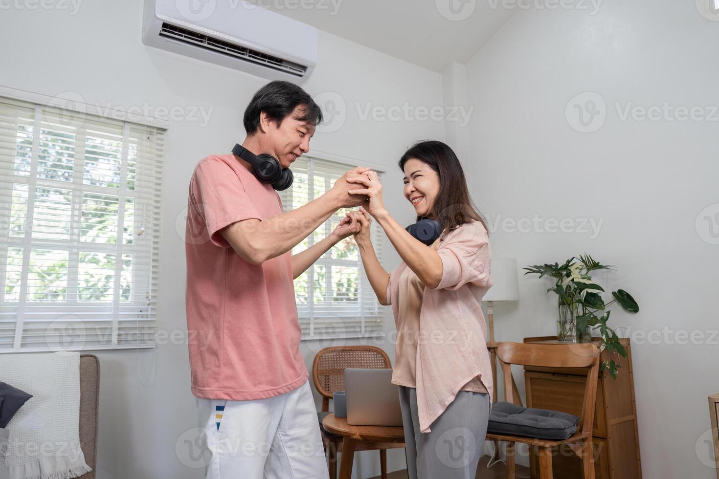 Happy middle-aged couple dancing together and holding hands indoors with headphones. photo