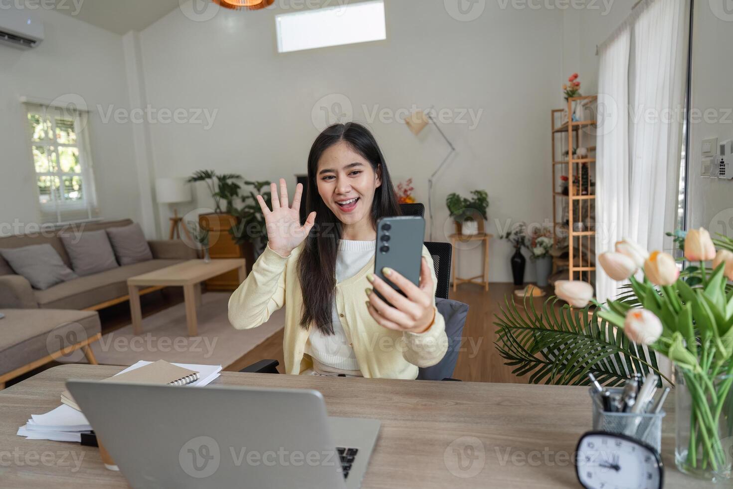 Young woman engaging in a call while working from home, smiling and waving at the camera. photo
