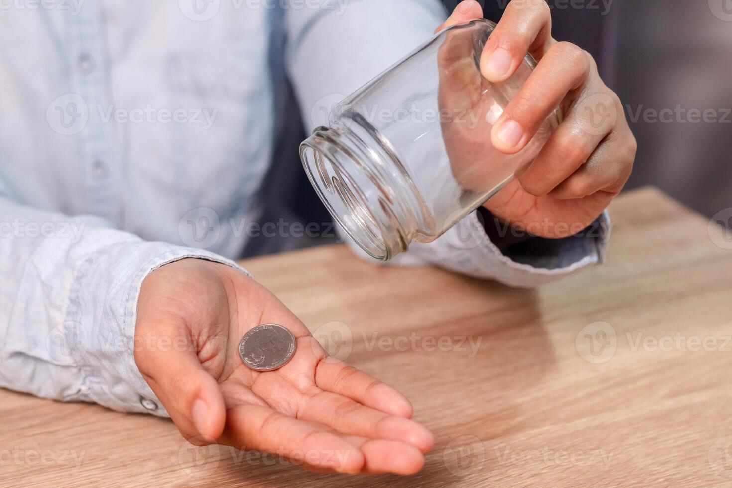 A woman pours a coin from a glass jar into her palm. Poverty concept. photo