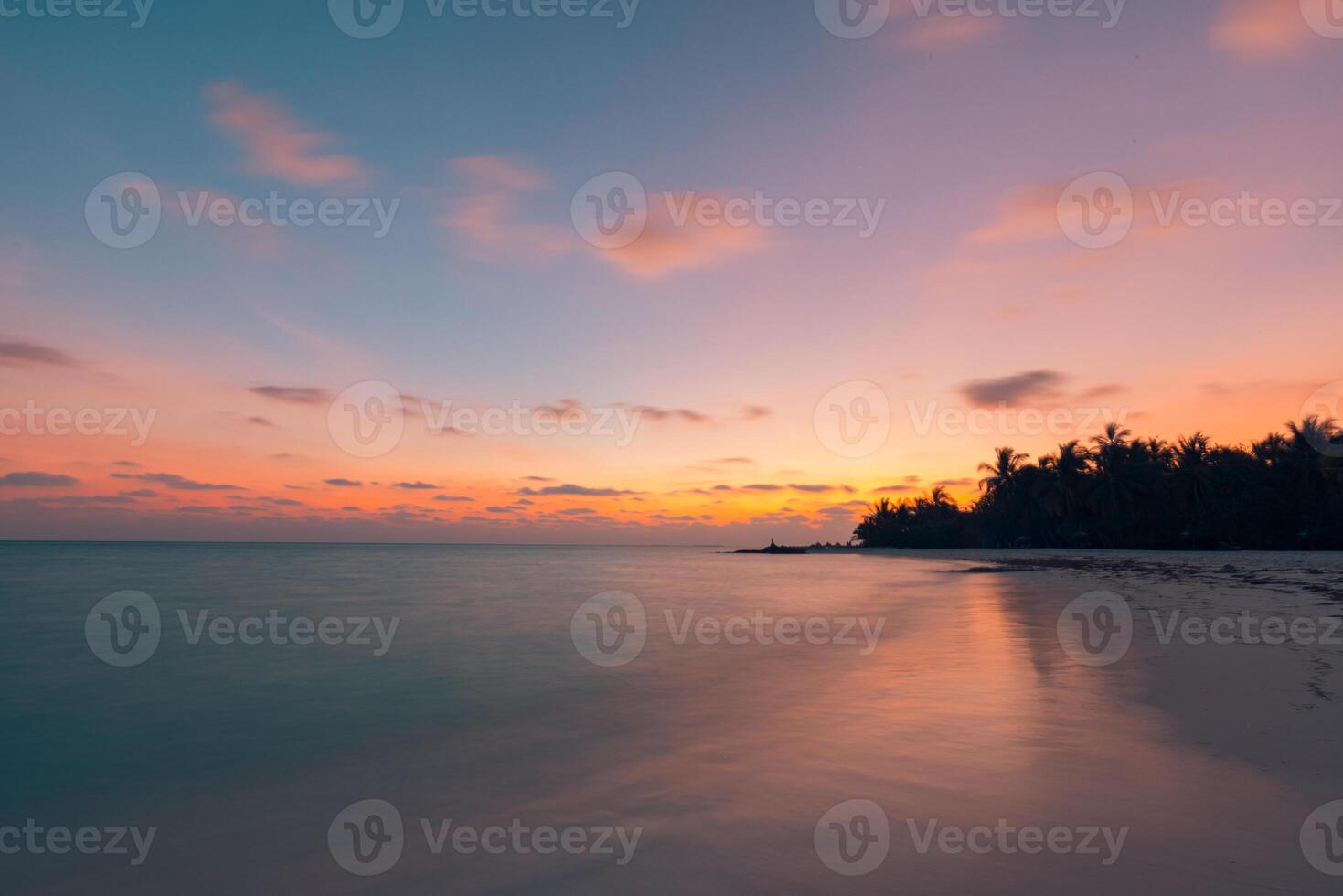 Serene sunset over tranquil island beach with silhouetted palm trees gently swaying against the vibrant sky calm sea water mirroring warm colors forming perfect tropical paradise for relaxation photo