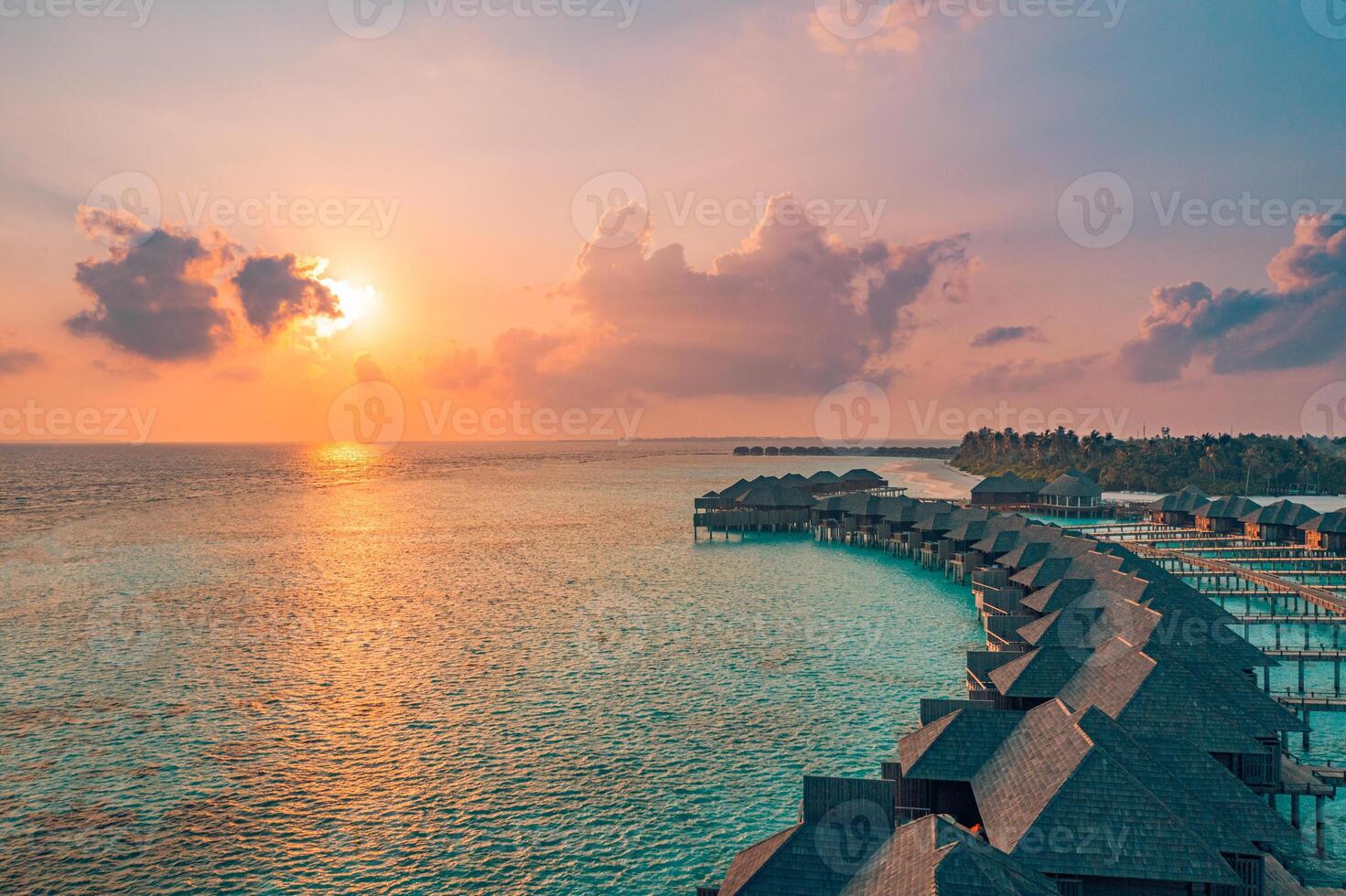 Breathtaking sunset aerial view of Maldives island with overwater villas stretching across a turquoise lagoon surrounded by white sandy beaches serene tropical paradise for luxury relaxation escape photo