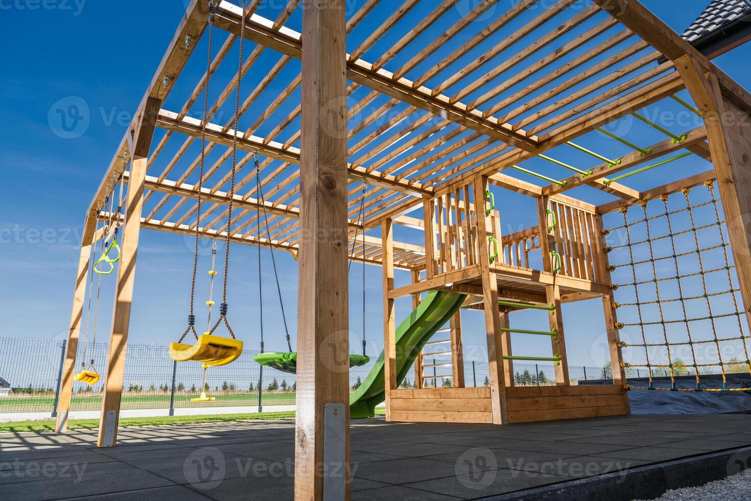 Modern Wooden Playground Structure Featuring Swings, Slide, and Climbing Wall Against a Clear Blue Sky in a Recreational Area photo