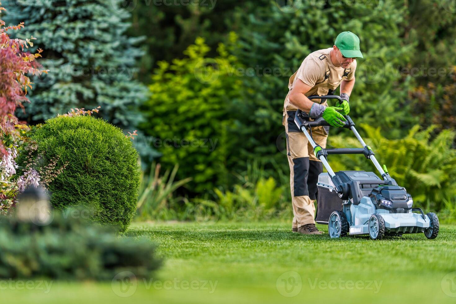 Man Mowing Grass in a Lush Garden on a Sunny Day With Vibrant Greenery and Well-Maintained Plants photo