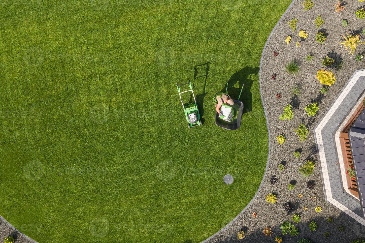 Man Mowing a Lush Green Lawn in a Well-Maintained Garden Under Bright Sunlight During Summer photo