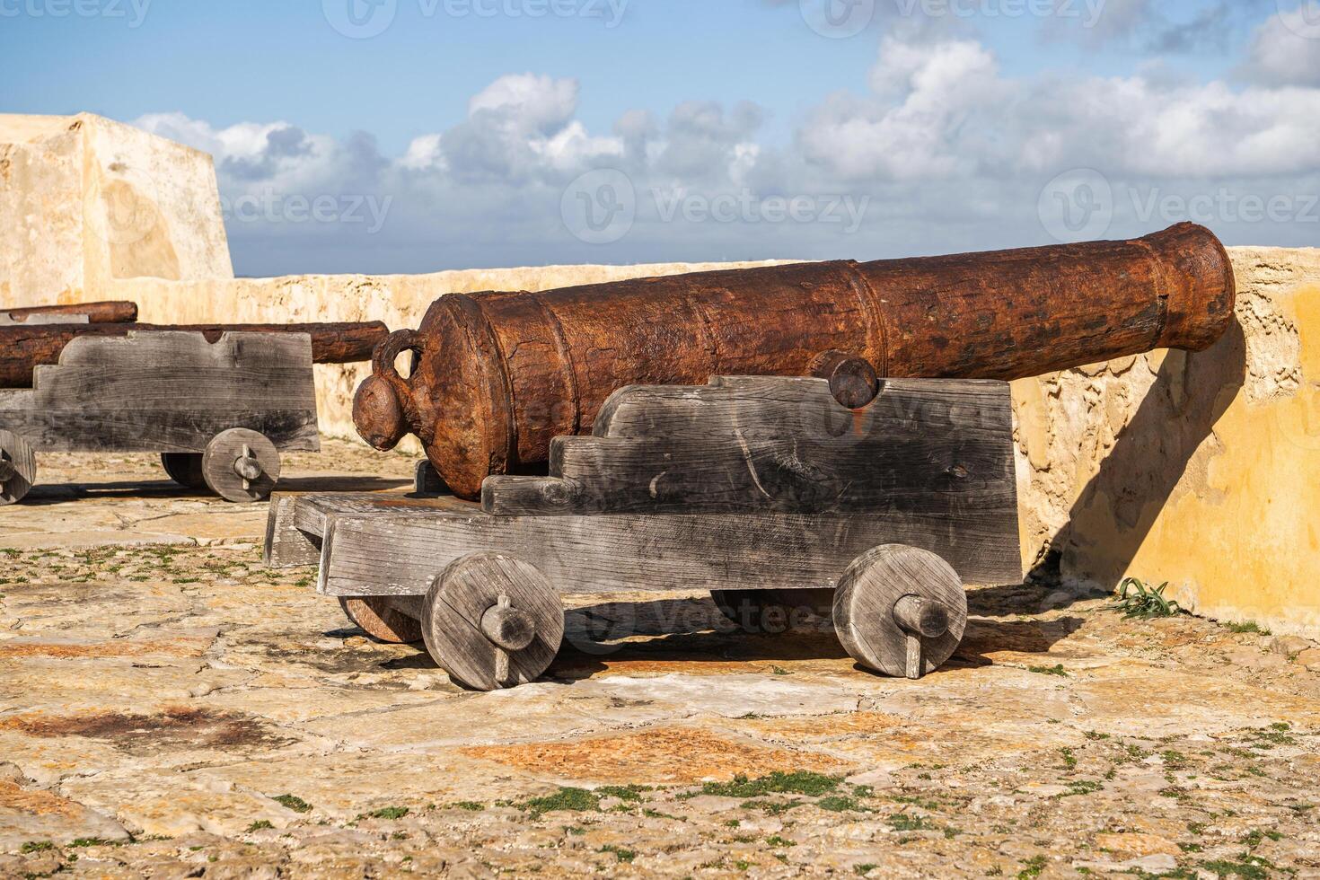 Historic Cannon Stands on Stone Ground at a Fort in Bright Sunlight With a Clear Blue Sky and Clouds photo