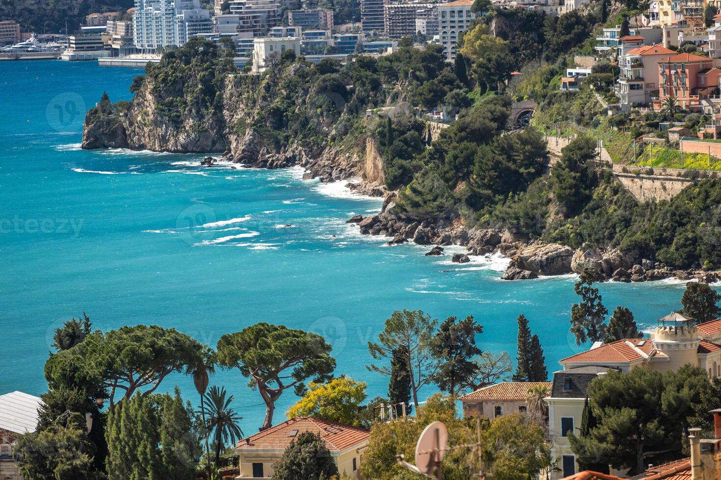 March 15, 2025 Monte Carlo, Monaco. Coastal Landscape With Clear Turquoise Waters and Rocky Cliffs in a Sunny Mediterranean Setting Near an Urban Area photo