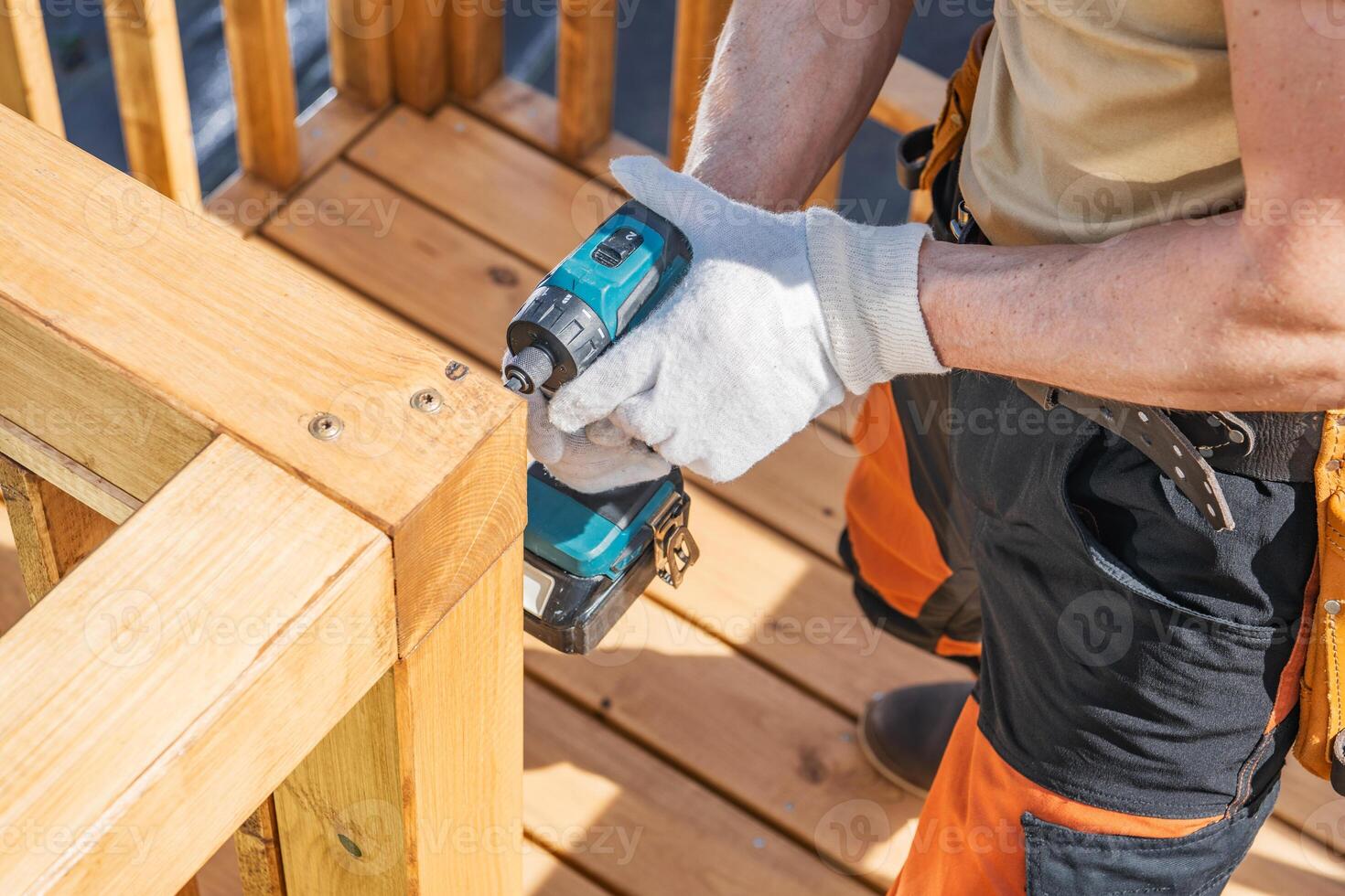 Person Using a Cordless Drill to Secure Wooden Railing on a Sunny Day at a Construction Site photo
