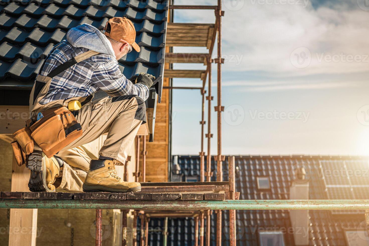 Construction Worker Inspecting Tools While Kneeling on Scaffolding at a Building Site During Sunset photo