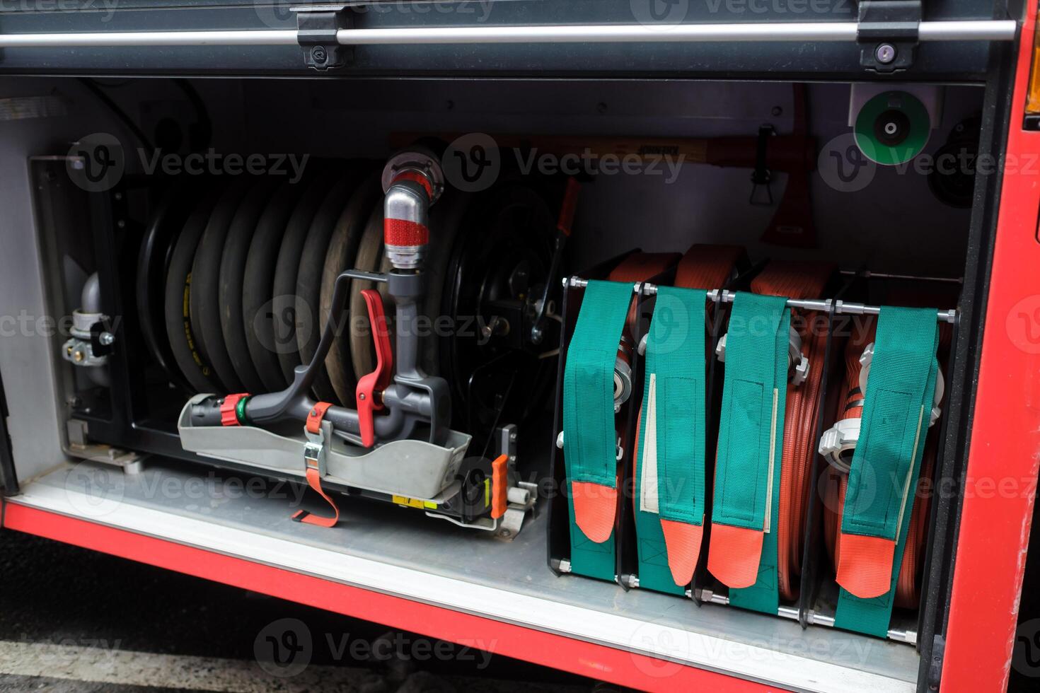 Equipment used for firefighting is neatly organized in a fire truck compartment with hoses, valves, and control panels present in the background during daylight hours. photo