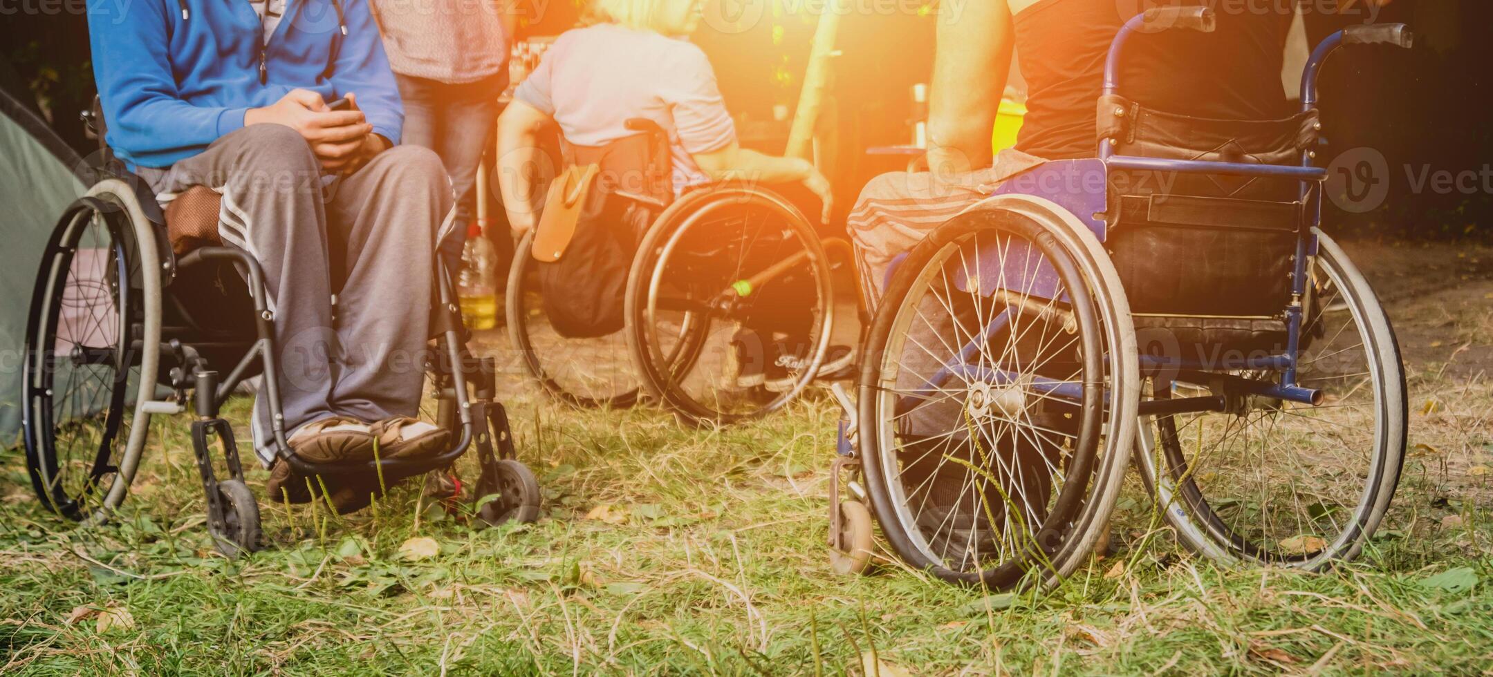 Two disabled men resting in a campsite with friends. Wheelchair in the forest photo