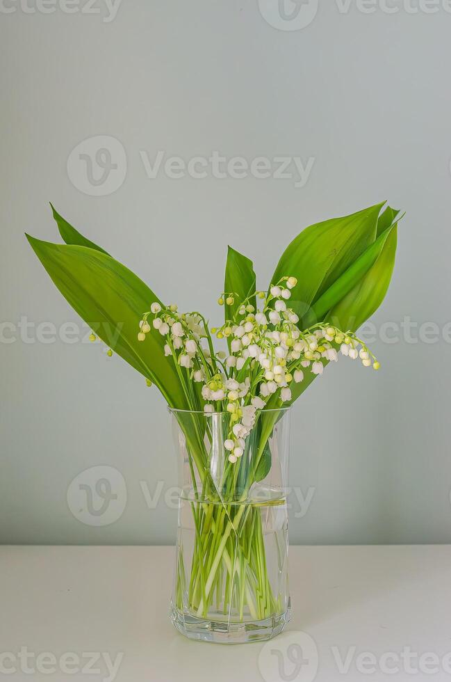 Beautiful lily of the valley flowers arranged in a clear vase with green leaves. High quality photo