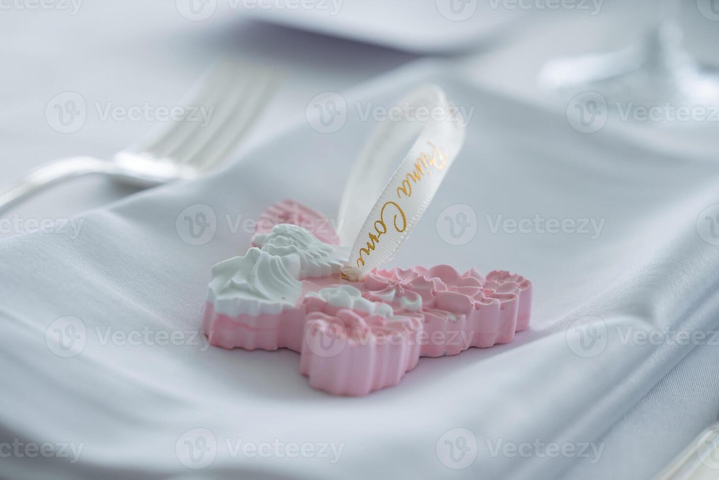Decorative cross shaped ornament with floral details and angel motif on a folded napkin, with a fork and glass in a refined dining setting. photo
