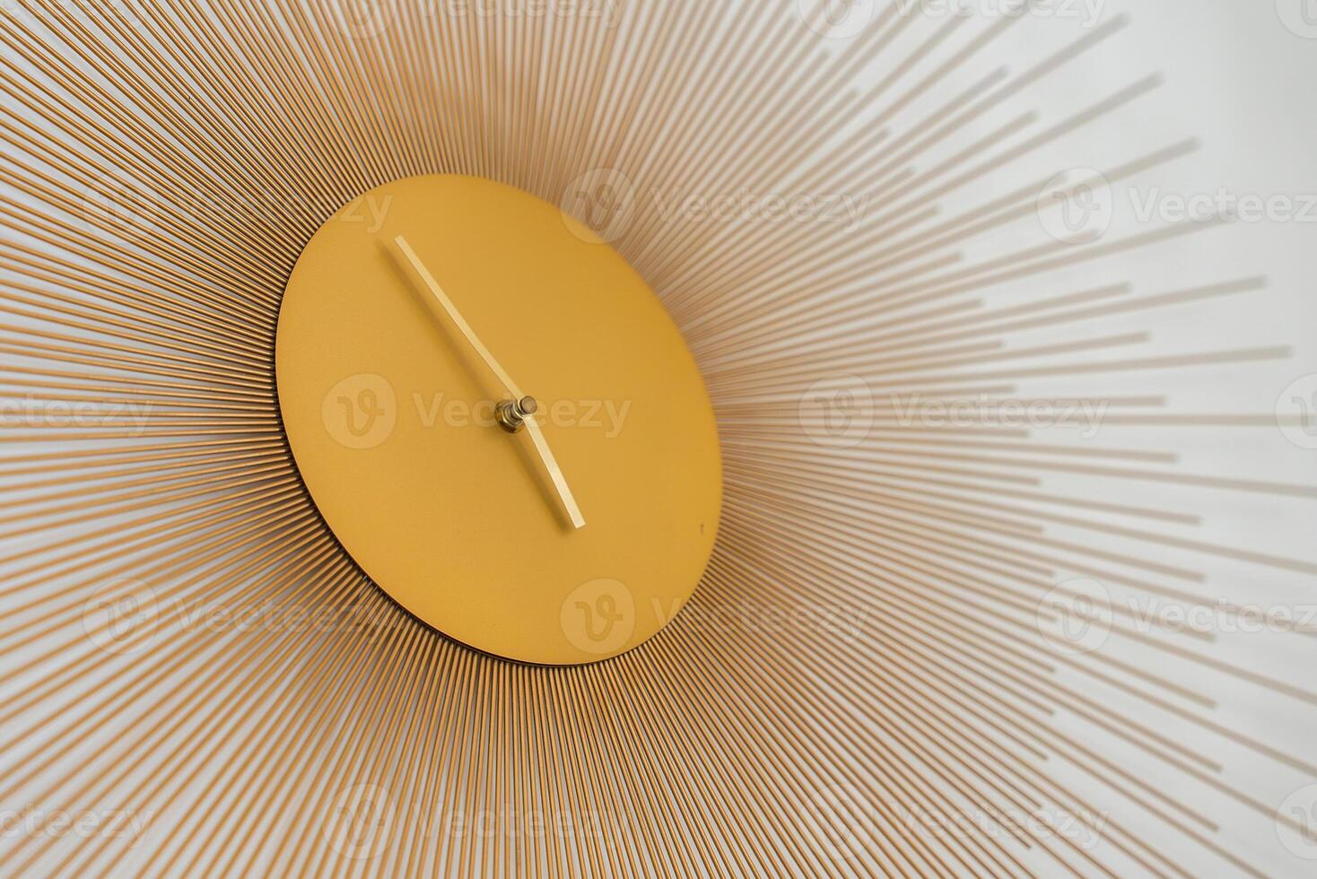 A modern wall clock with a golden circular face, minimalist hands, and radiating metal rods, mounted on a plain white background. photo