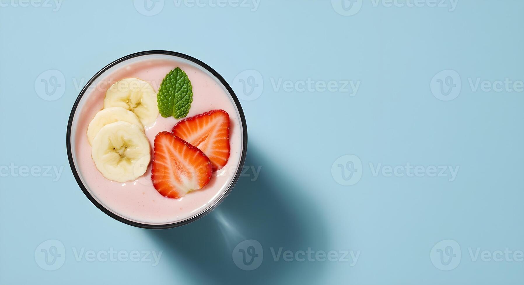 A refreshing smoothie bowl with vibrant strawberries, banana slices, and mint against a blue backdrop. photo