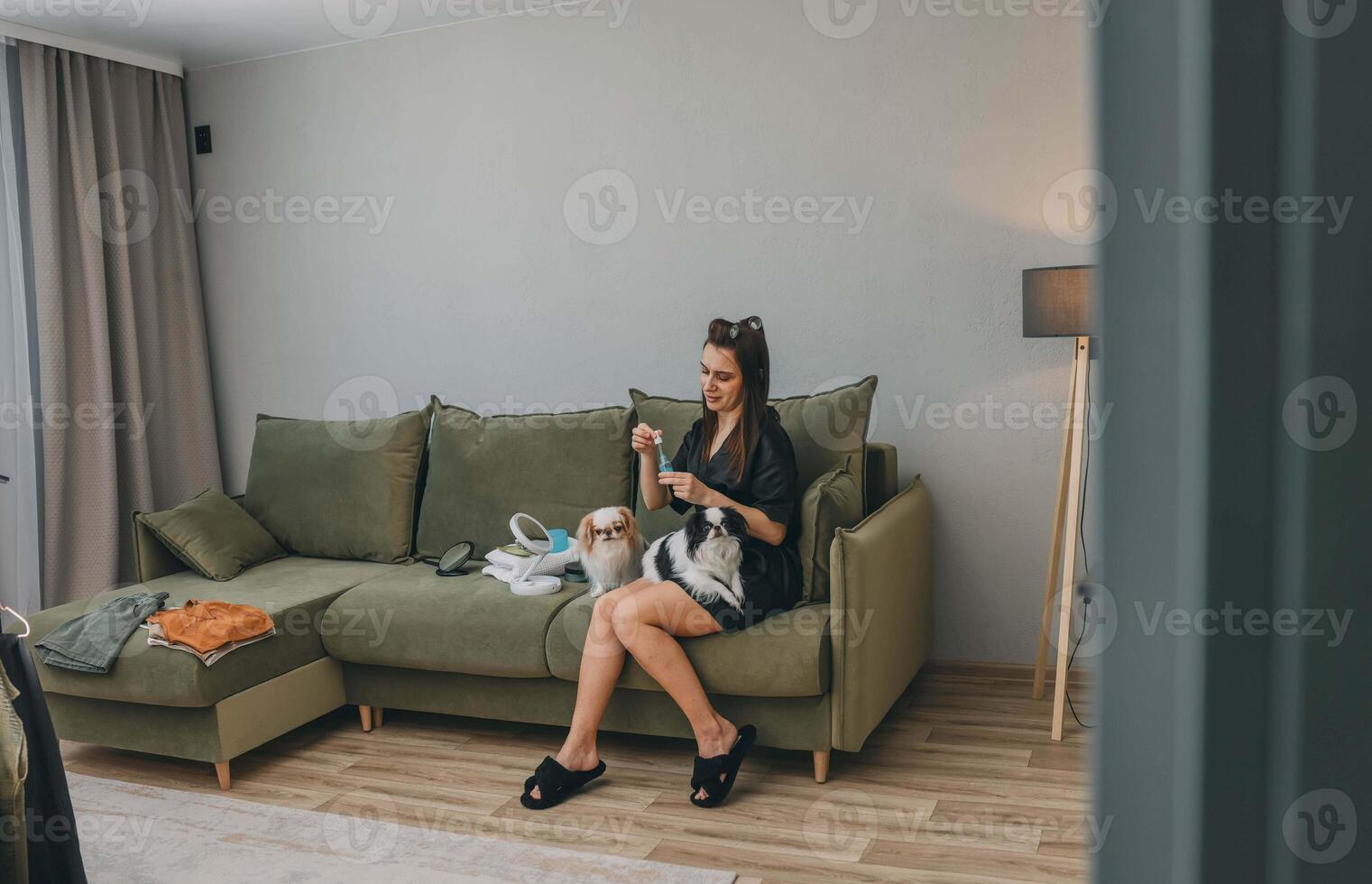 woman with pet dogs at home, applying beauty product in living room setting concept of daily life, pet care, personal grooming photo