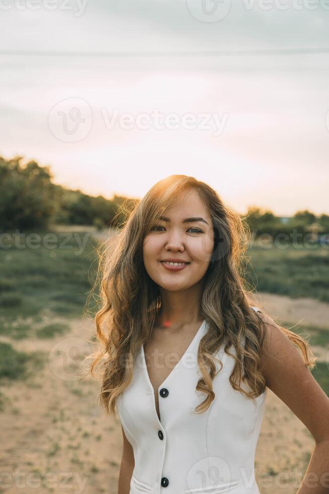 young Asian woman in white vest during sunset on rural path, soft golden light highlights her hair and creates a warm glow, concept of personal branding, wellness, natural beauty photo