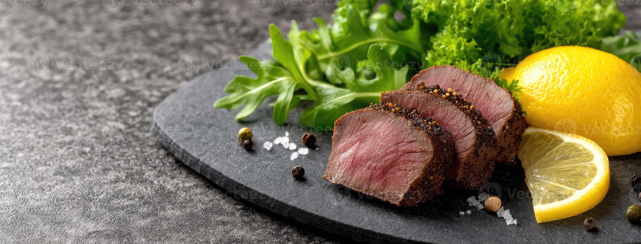 A piece of meat with lemon and herbs on a black plate photo