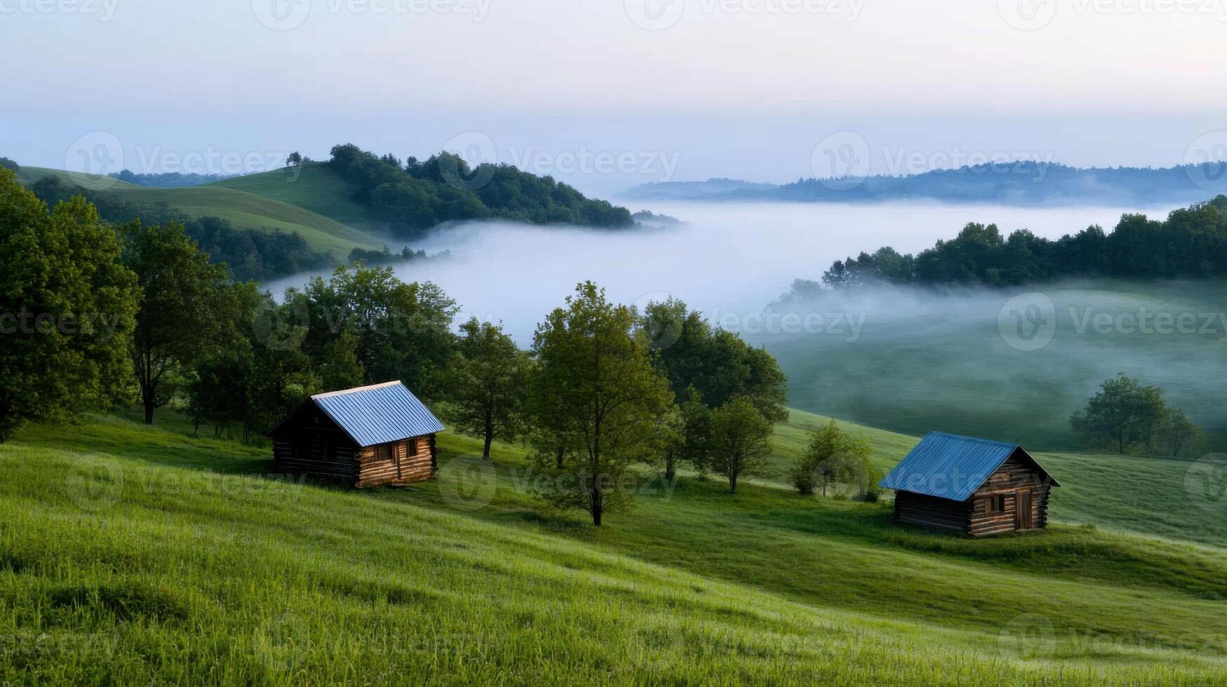 Early morning mist blankets rolling hills where two rustic cabins sit peacefully. The lush green grass and trees create a tranquil atmosphere, inviting exploration photo
