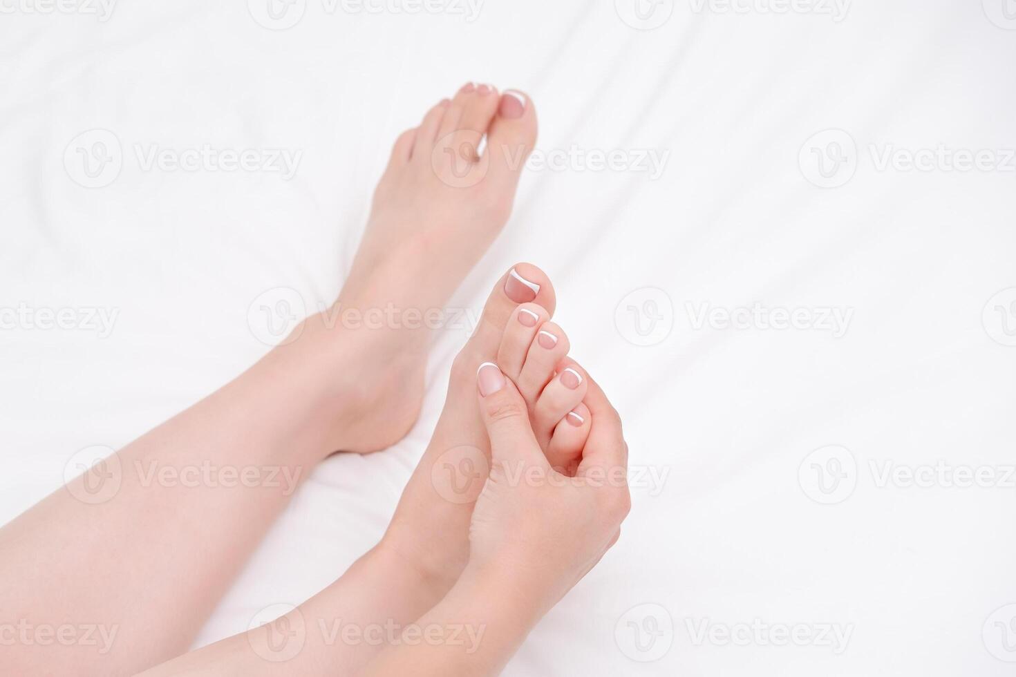 female legs and hands with beautiful manicure and pedicure on white sheet close-up photo