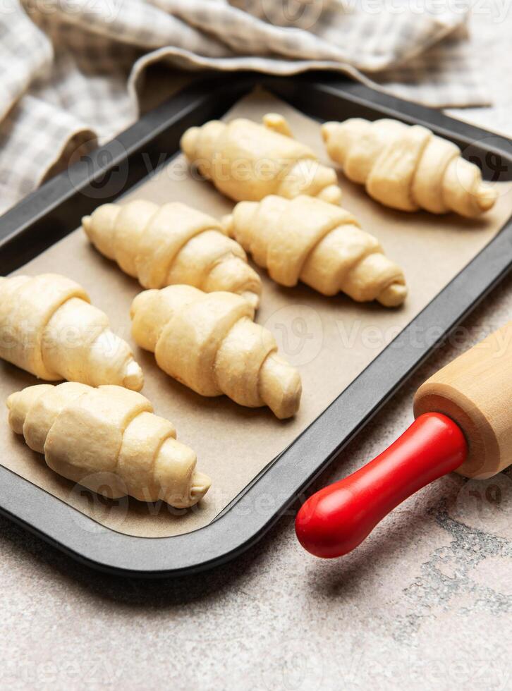 Raw croissants baking on tray with rolling pin and a towel photo