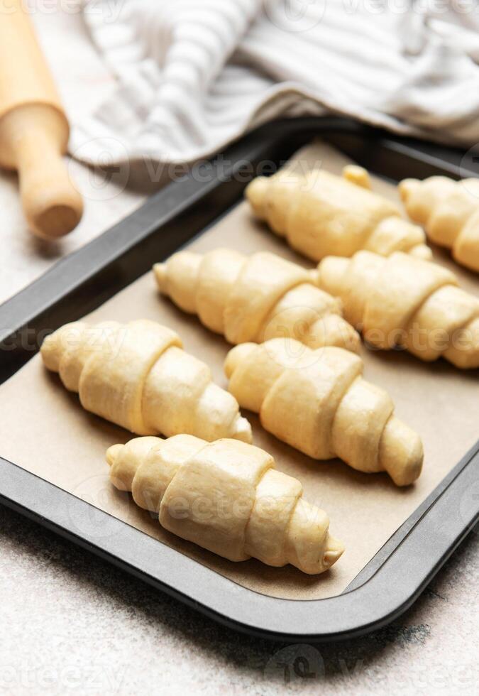 Raw croissants baking on tray with rolling pin and towel photo