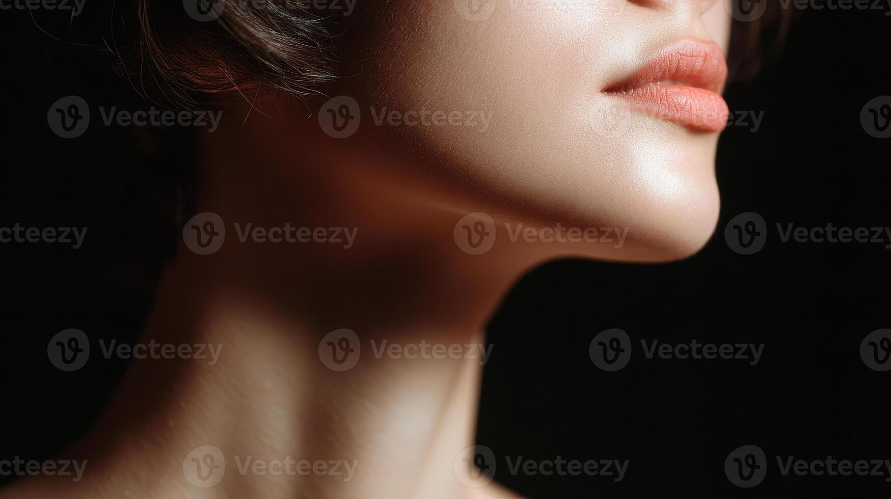 Soft light highlights smooth skin and delicate lips of woman neck and jawline in close up portrait with dark background photo