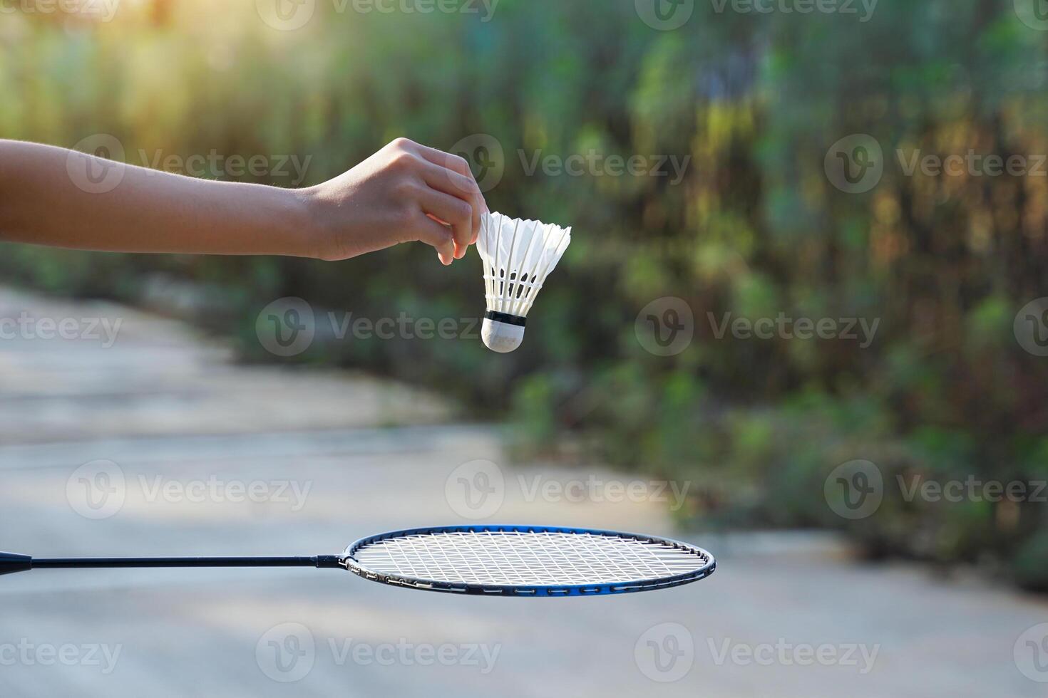 hand holding a white shuttlecock to release into the badminton racket below. Soft and selective focus. photo