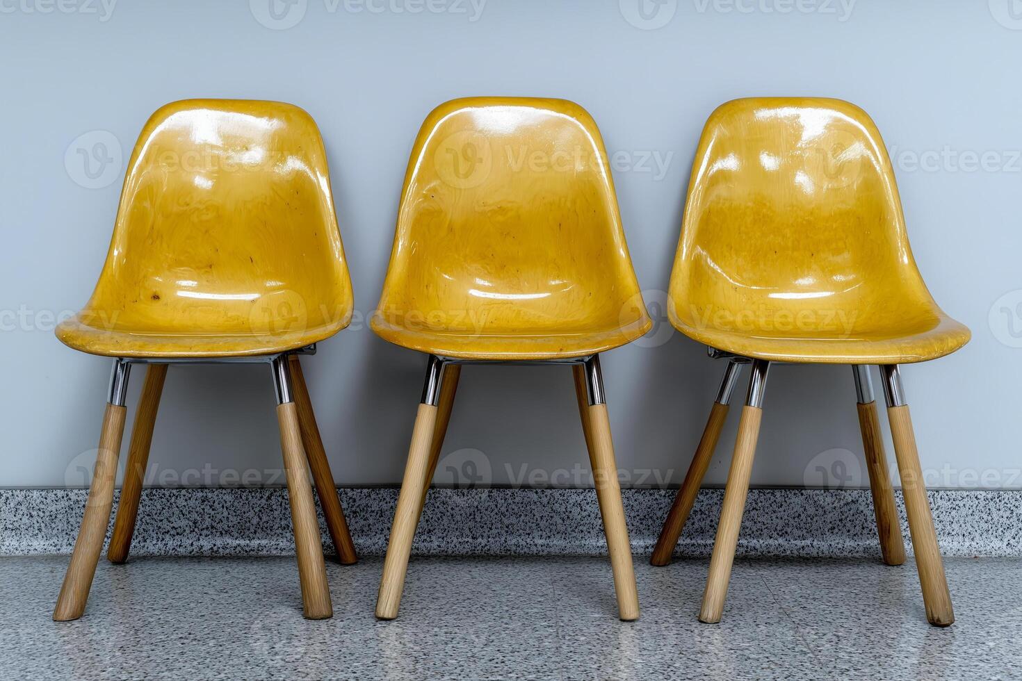 Three vintage yellow chairs with smooth, glossy surfaces and wooden legs are arranged in a straight line against a light gray wall, showcasing a minimalist design. photo