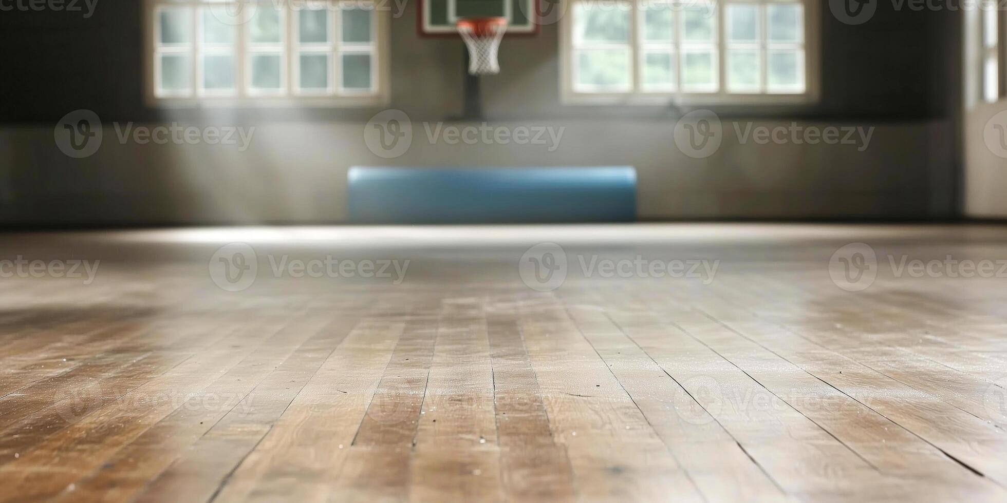 A wooden basketball court floor is seen from a low angle, with sunlight streaming through windows. The hoop is visible in the background, adding depth. photo