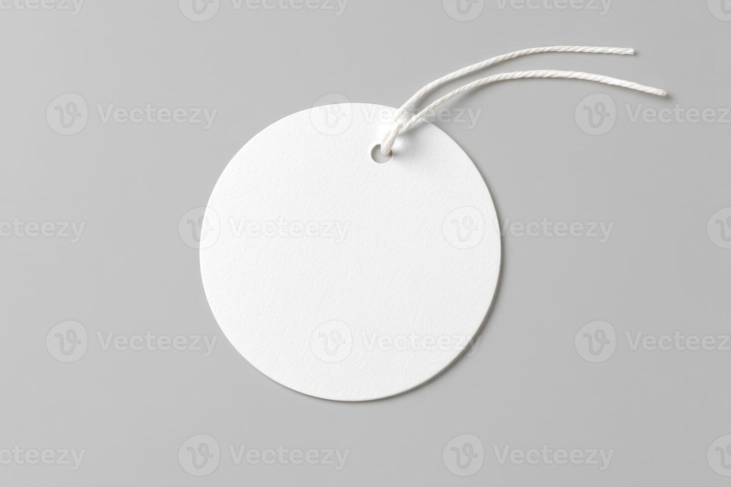 A blank, round, white tag with a string hanging against a gray background, emphasizing its simplicity and space for customization. photo