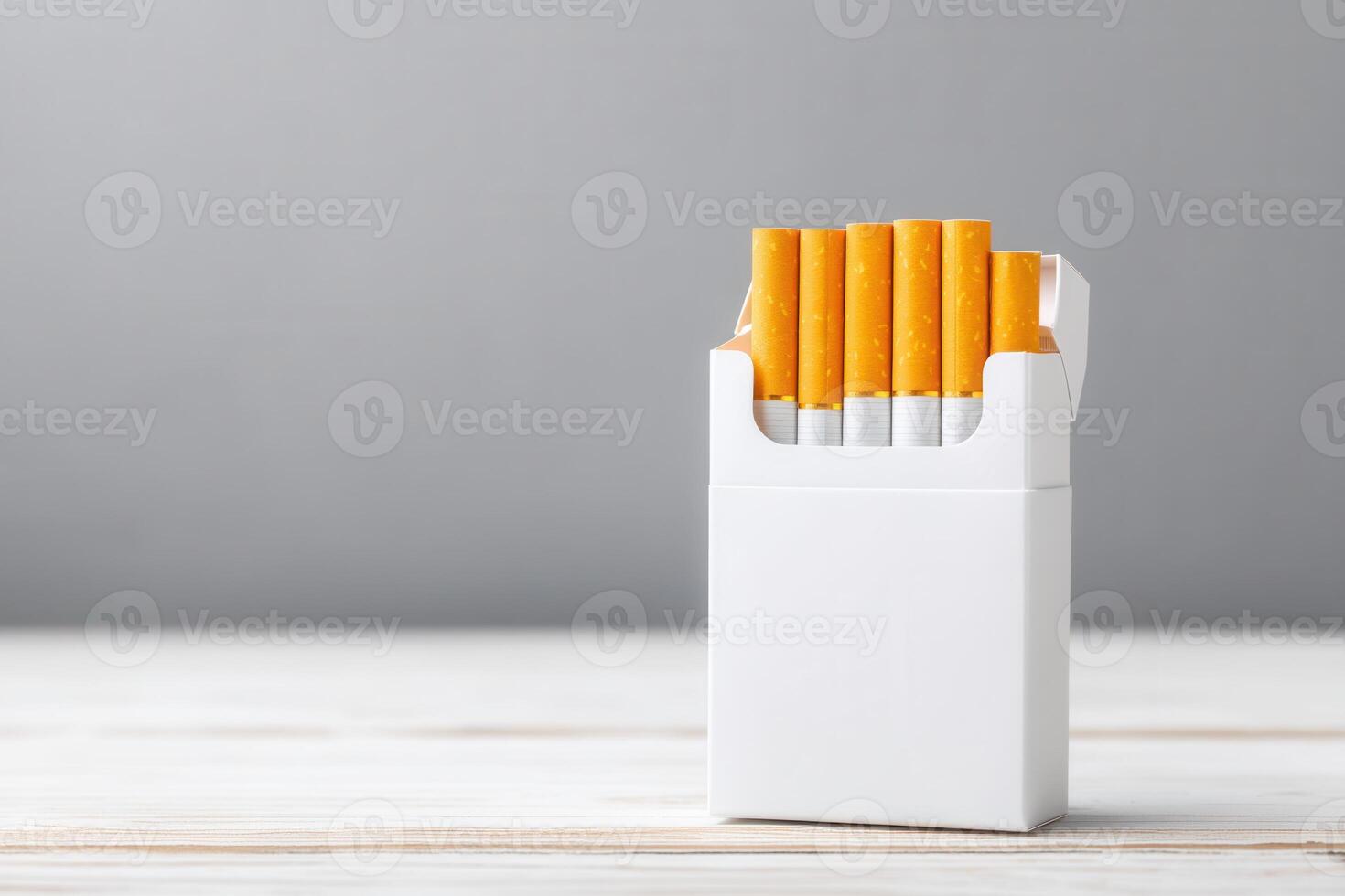 A full packet of cigarettes with white filters and orange tips. Packaged on top of a white wooden table against a gray background. photo