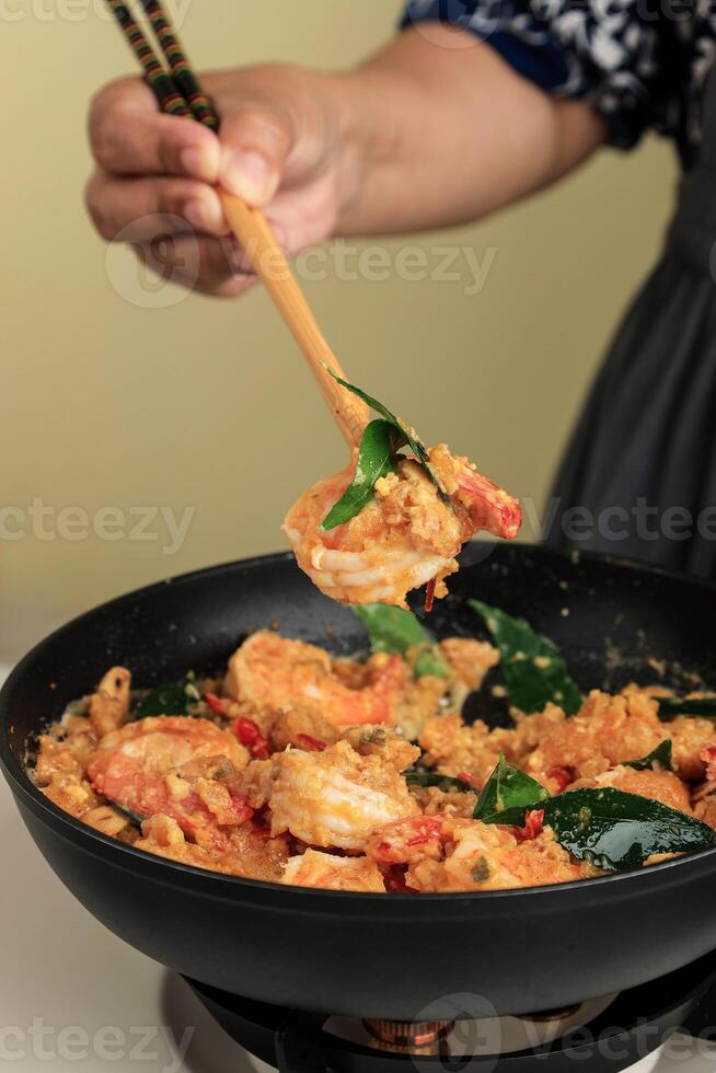 Female Hand Cooking Shrimp with Salted Egg Sauce using Long Chopstick on Black Pan photo