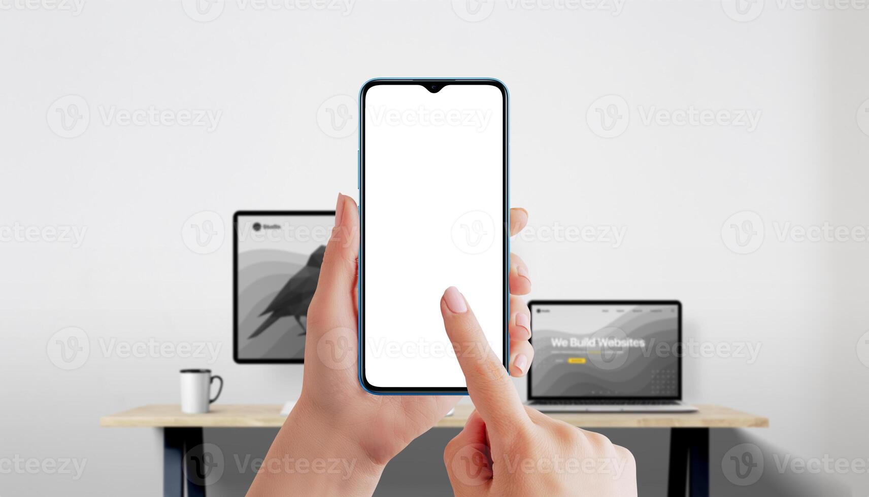 Smartphone mockup in female hands with finger touching white screen, office background with laptop and monitor photo