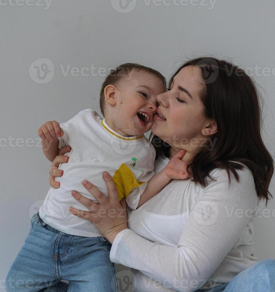 A young mother and her son are captured mid-laugh in a bright, white photo studio. The mother is playfully spinning her son around