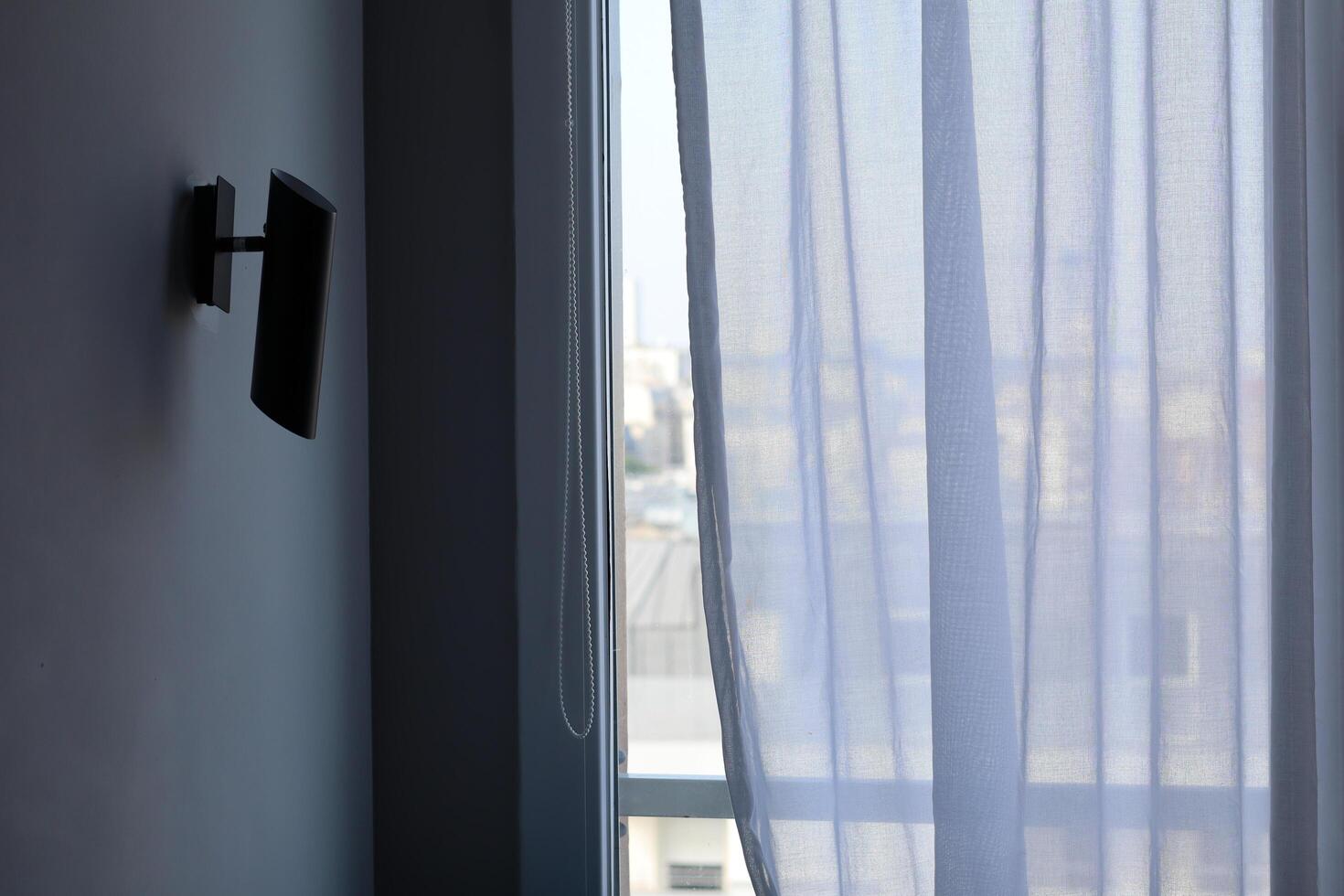 Soft curtains gently sway in the breeze, revealing a sunlit city view from an indoor space photo