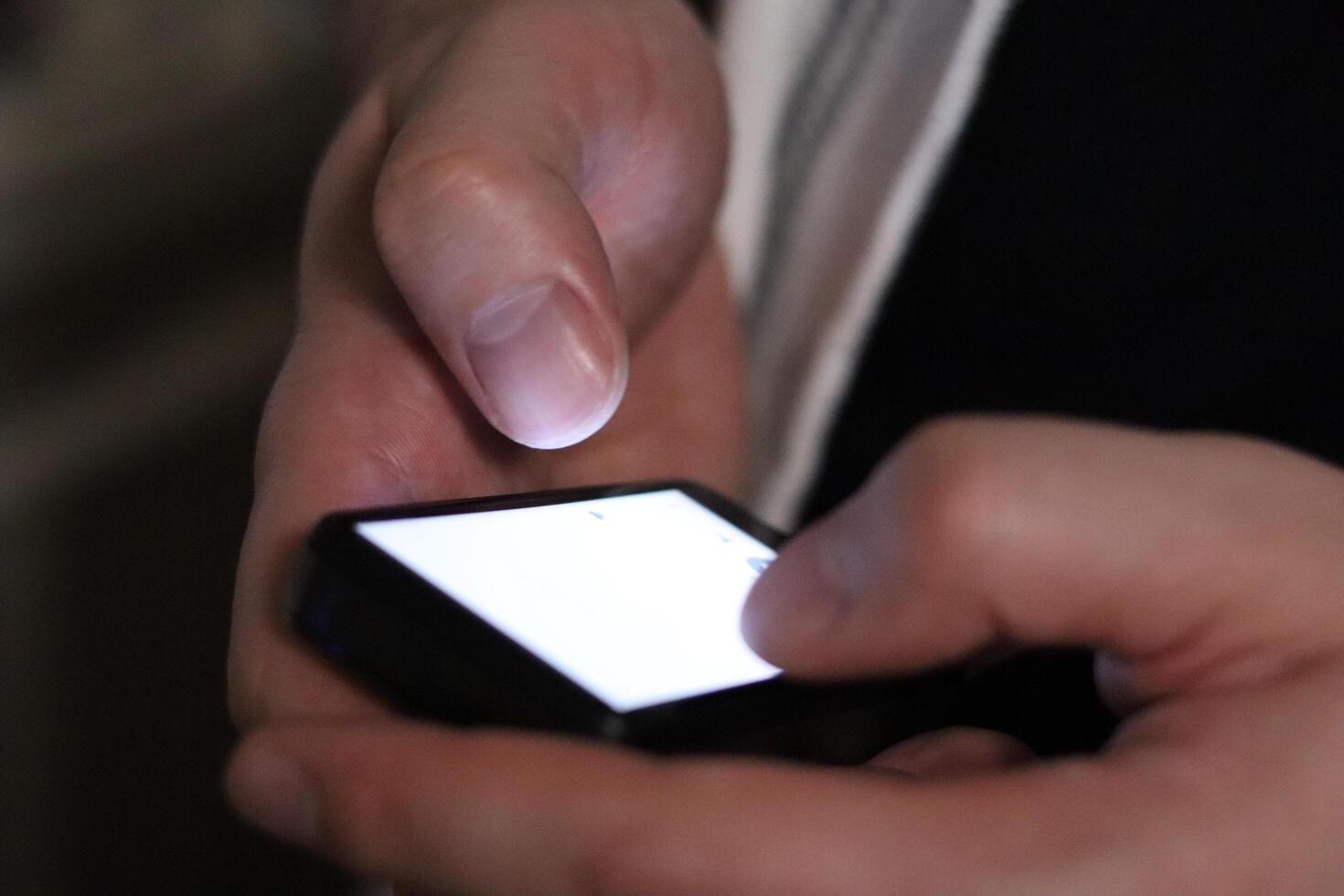 Hands using smartphone in dark indoor setting while engaging with digital content photo