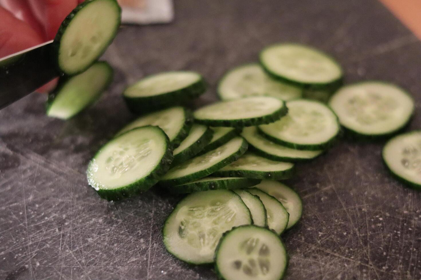 Fresh cucumber slices being cut on a wooden cutting board in a kitchen setting during meal preparation photo